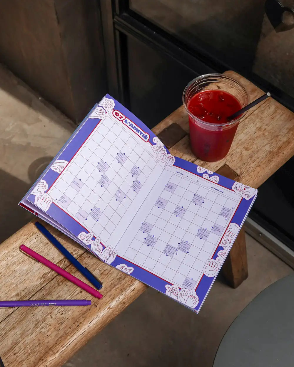 Cahier mots fléchés Grillé Amour avec grilles thématiques, stylos colorés et verre de jus sur table
