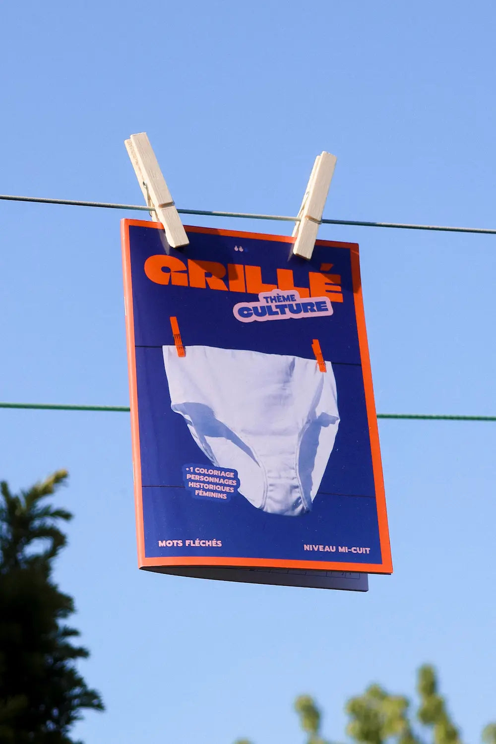 Cahier Grillé Culture mots fléchés thème culture suspendu à pinces sur fil, packaging bleu et orange
