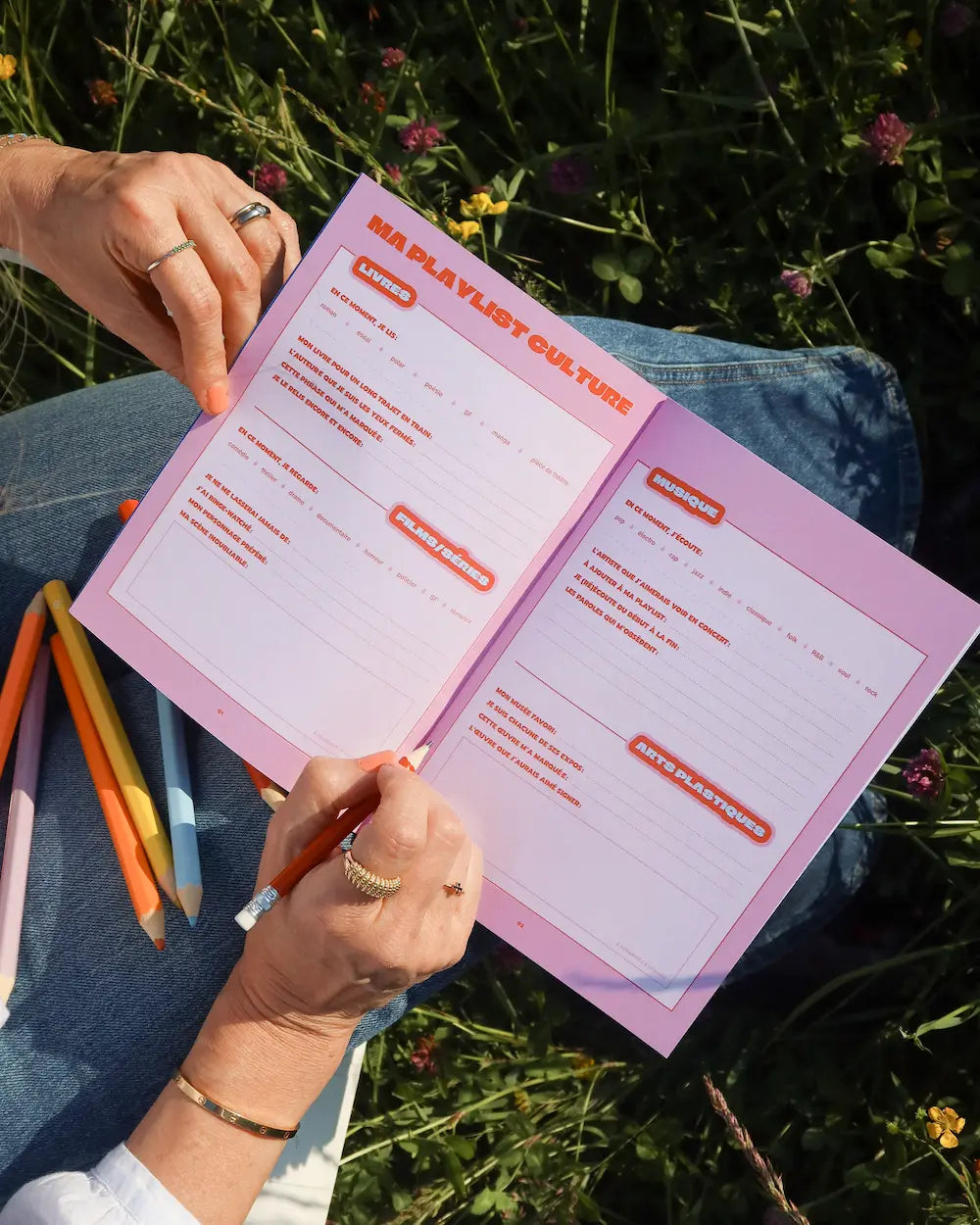 Cahier Grillés CULTURE rose avec mots fléchés pop culture, tenu en main en extérieur parmi les fleurs