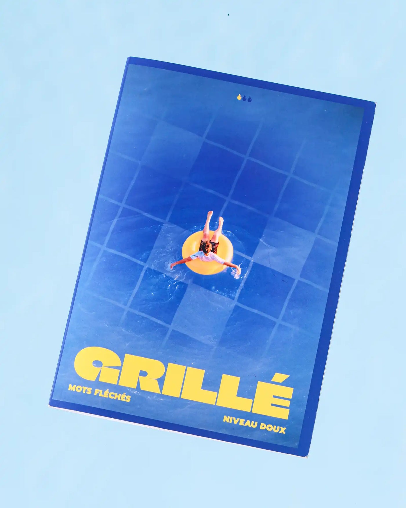 Cahier mots fléchés Grillé Tout Doux niveau facile, couverture bleu avec illustration colorée d'une personne sur anneau gonflable jaune