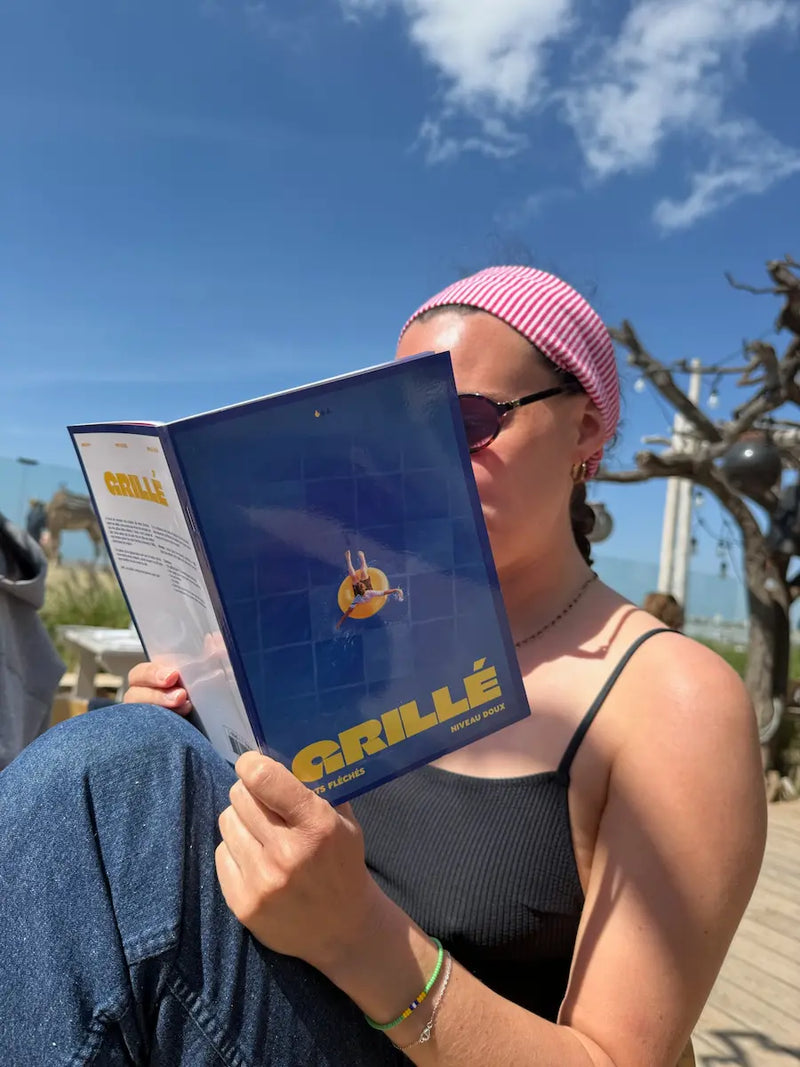 Femme en rose tenant un cahier Grillé bleu au soleil devant des cactus, illustration jeu mots fléchés