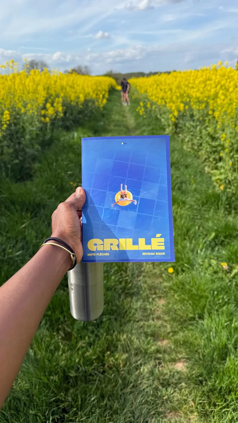 Cahier Grillé niveau doux tenu en main dans un champ de colza jaune vif