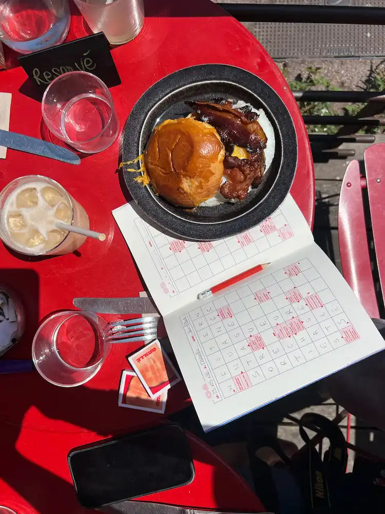 Cahier Grillé avec burger et bacon servi dans une assiette, verre d'eau et stylo sur table rouge
