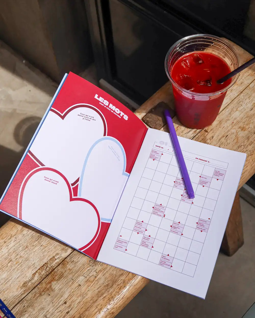 Cahier mots fléchés Grillé Collection Amour rouge ouvert avec grilles remplies, stylo violet et verre de jus rouge