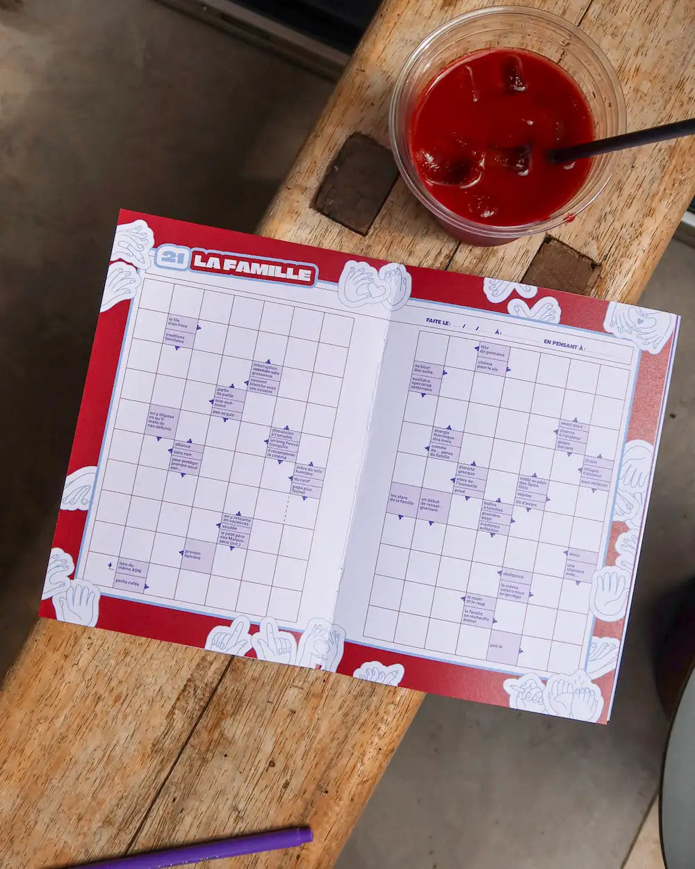 Cahier mots fléchés Grillé thème Amour ouvert sur grille avec stylo et verre de jus rouge