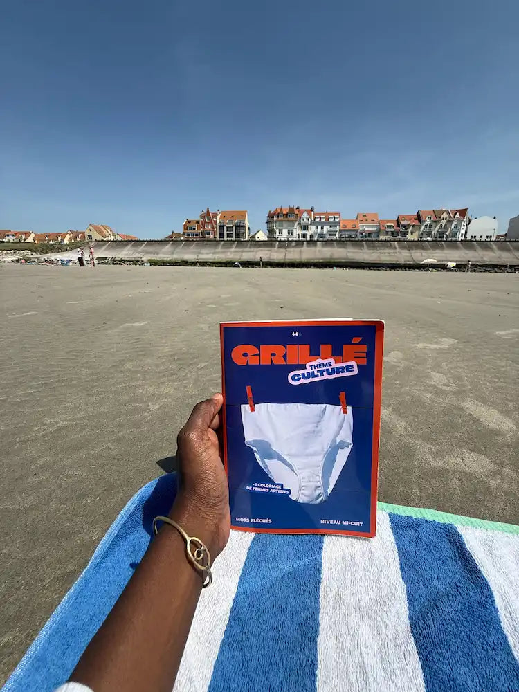 Cahier Grillé tenu à la main sur une plage avec une dike en arrière plan